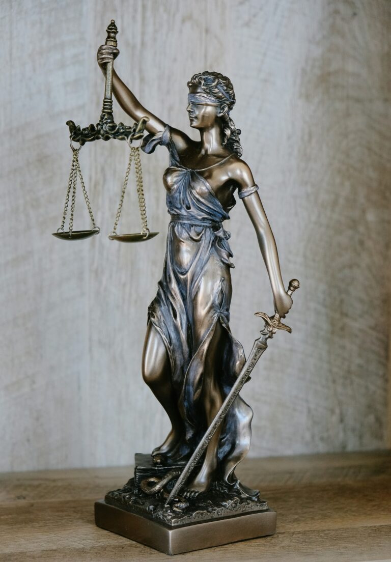 Lady Justice statuette on a wooden table against a grey background